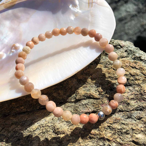 Sunstone 6mm Bead Bracelet with a shell and rocks behind